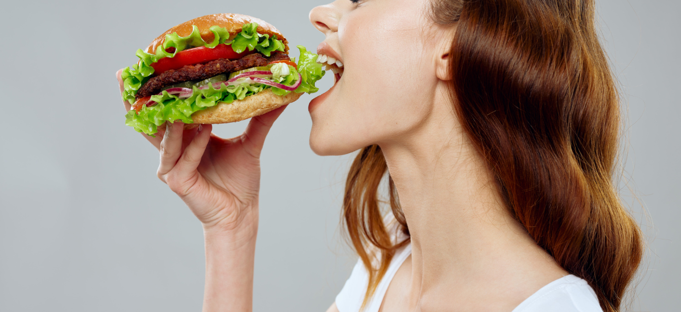 Perfil de uma mulher jovem a dar um dentadad num hamburger