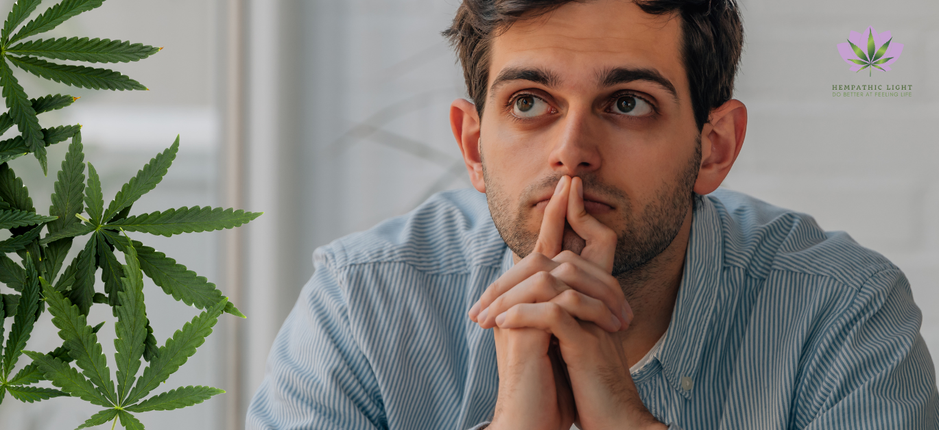 Homem jovem  como o polegares unidos encostados á boca e restantes dedos entrelaçados, numa atitude introspectiva. Folhas de canábis naturais ao lado esquerdo da imagem