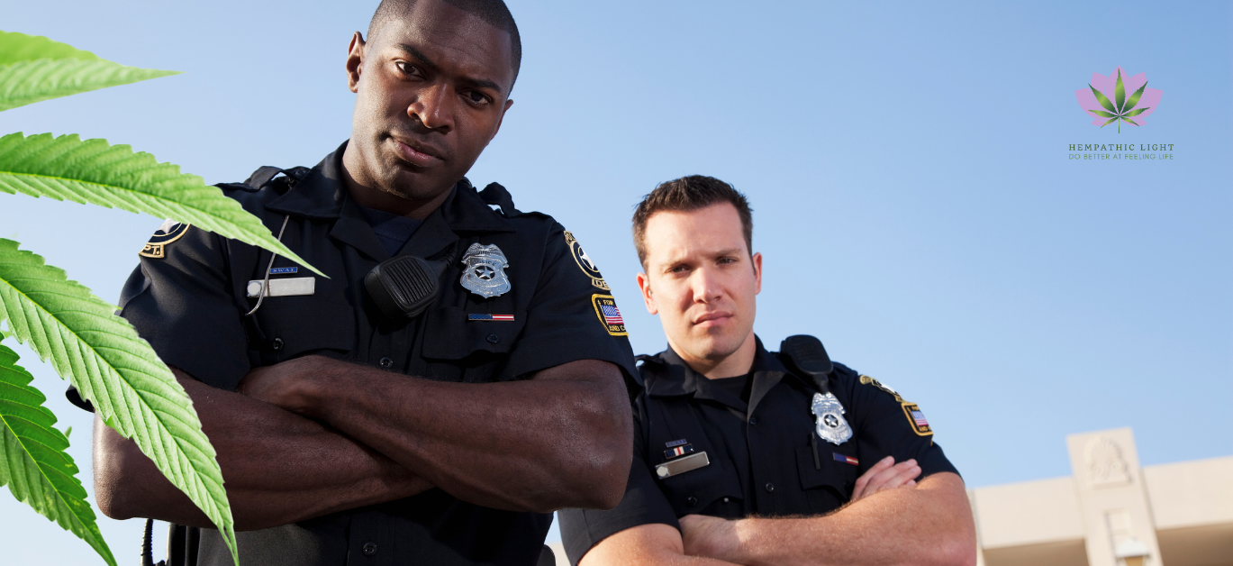 Dois policias de uniforme com os braços cruzados e numa postura inquisidora. Uma folha de canábis verde está sobreposta no lado esquerdo da imagem